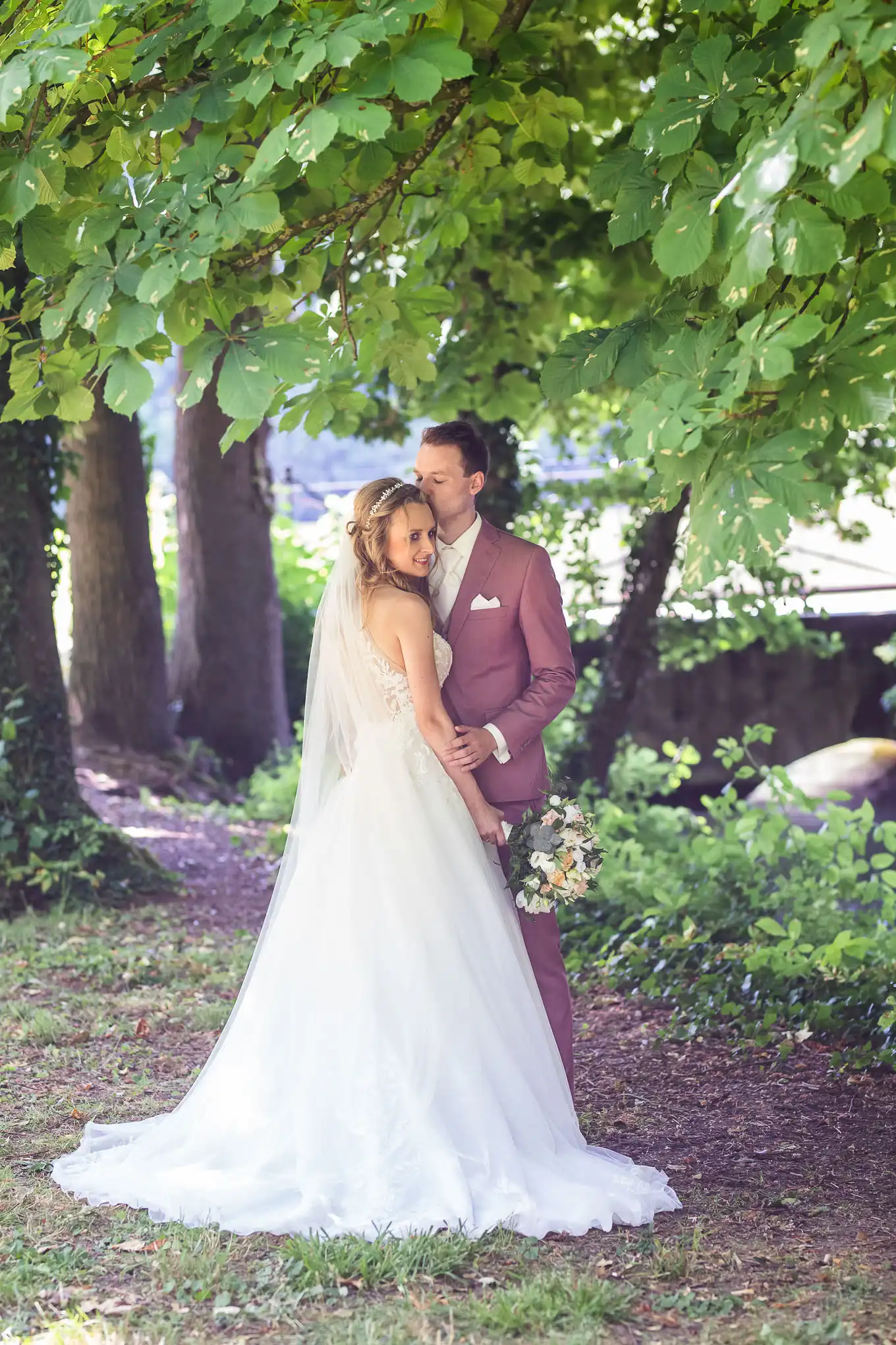 Bräutigam küsst Braut auf Stirn im Schlosspark Monrepos